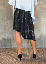 Load image into Gallery viewer, Back detail: this asymmetric Skirt-Pant is handcrafted from silk satin and blur the line between shorts and skirt. A deep, gathered waistband flows into a fluid silhouette, finished with a diagonal hemline that brings an unconventional edge to refined dressing.This  hand-drawn batik motif is inspired from the late 19th-century ‘Wiener Secession’ art movement, infusing the design with a refined sense of linear rigor softened by small foliage details. here in black background and steel grey motif.