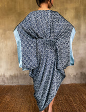 Load image into Gallery viewer, Back detail: asymmetric long Jogya silk dress with a "Deco" pattern in grey and dark blue colors. The dress features a loose fit with a belt and has a subtle asymmetrical design. Steel grey border define the kimono-like sleeves. Luxury resort-wear in silk batik made in Bali.