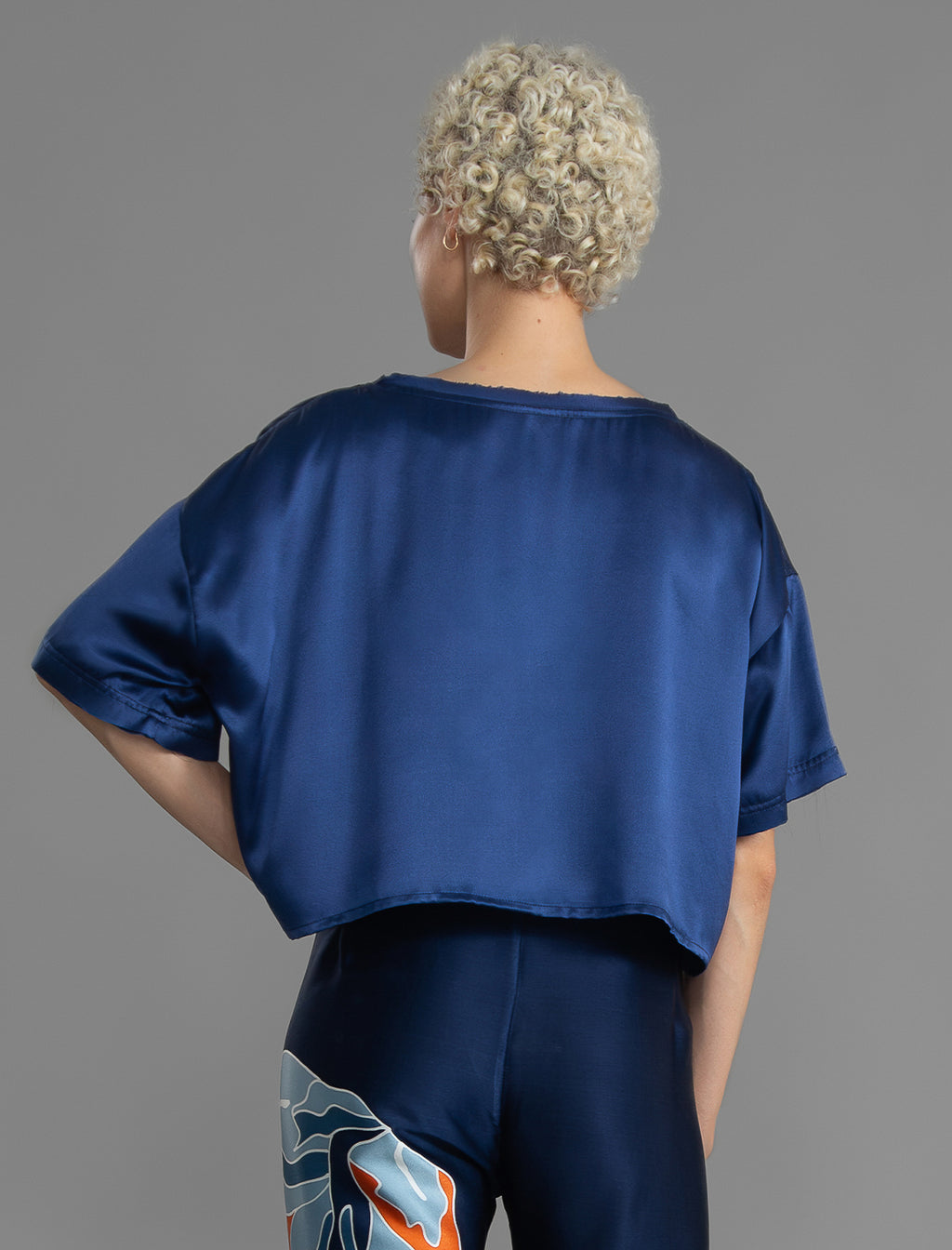 Back view. Slightly cropped boxy 100% silk stretch t-shirt in dark blue with raw cut detail on neckline and sleeves.