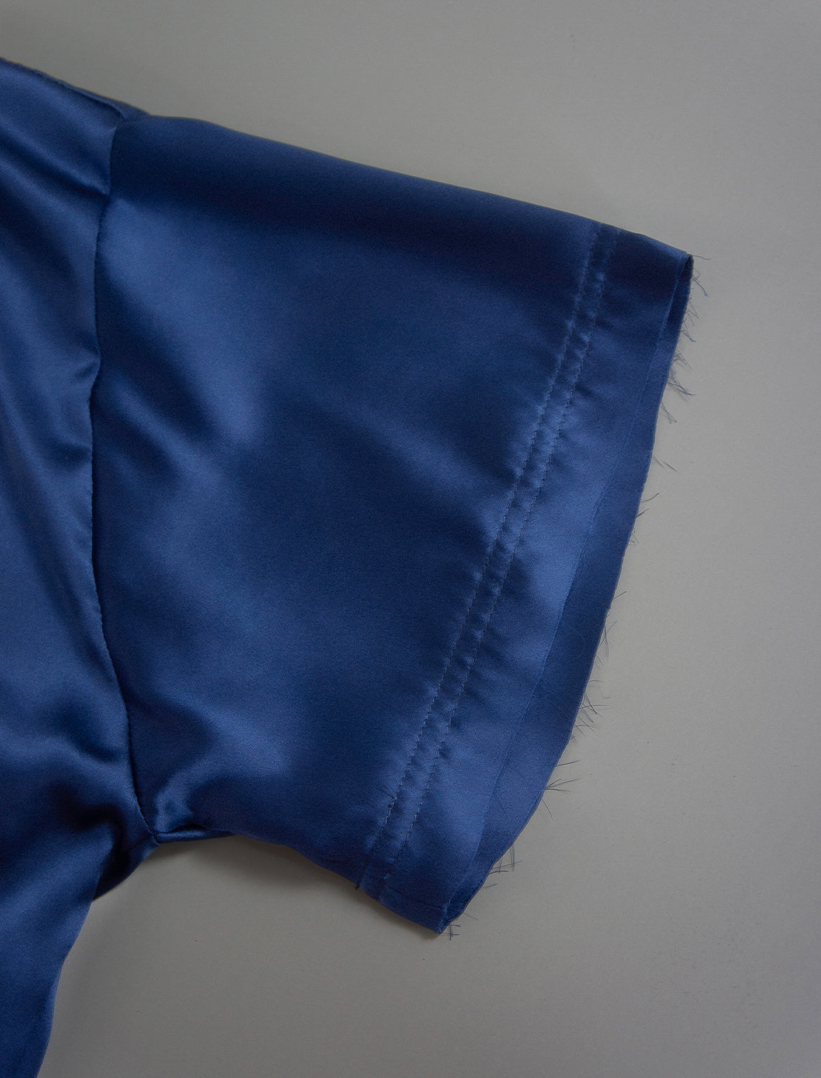 Sleeve detail. Slightly cropped boxy 100% silk stretch t-shirt in dark blue with raw cut detail on neckline and sleeves.