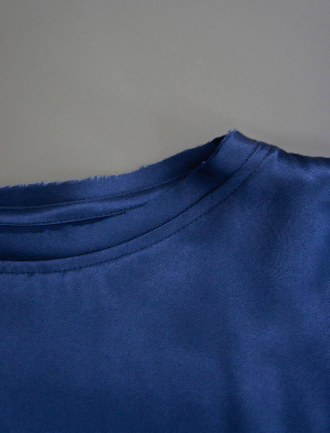 Neckline detail. Slightly cropped boxy 100% silk stretch t-shirt in dark blue with raw cut detail on neckline and sleeves.
