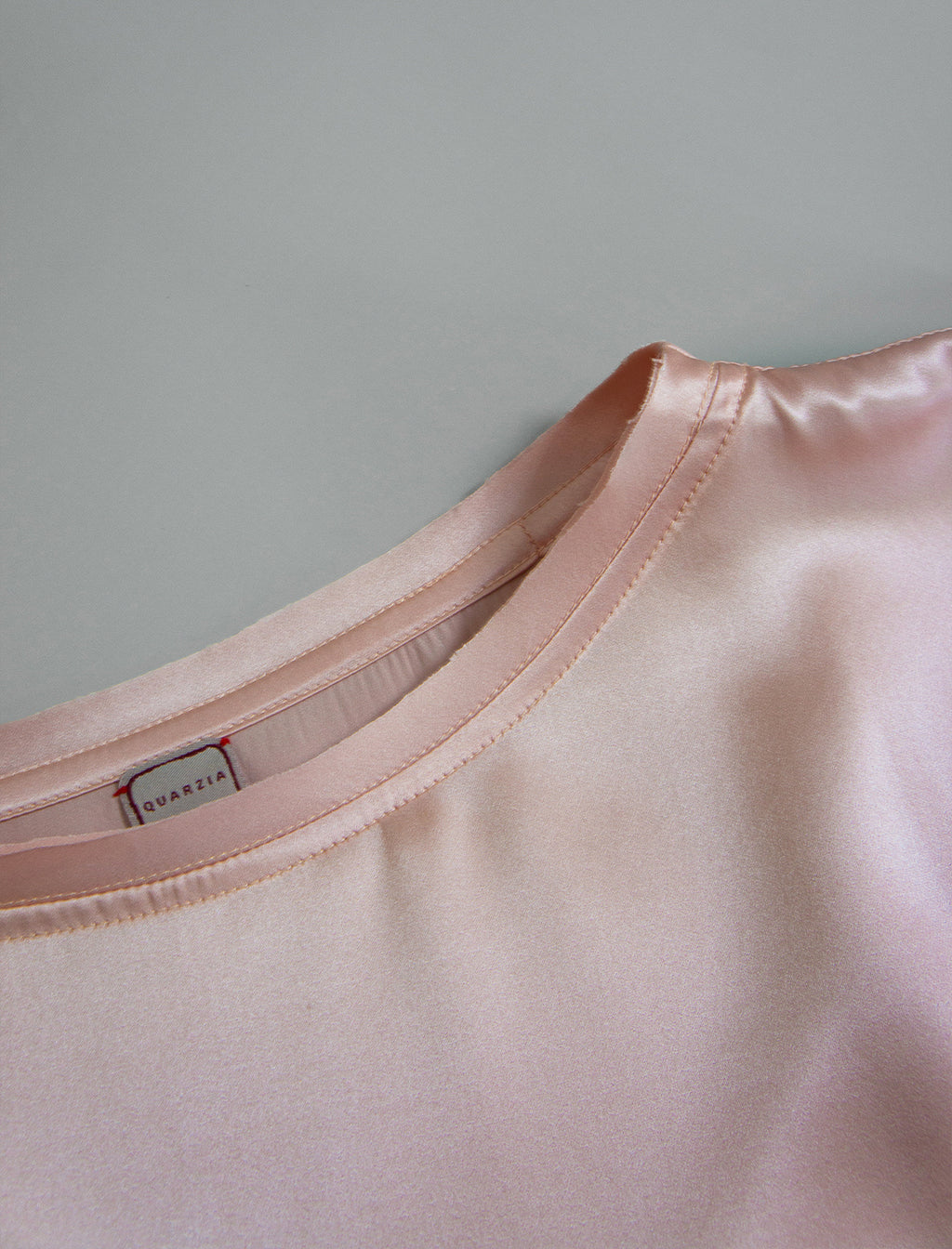 Neckline detail. Slightly cropped boxy 100% silk stretch t-shirt in soft pink with raw cut detail on neckline and sleeves.