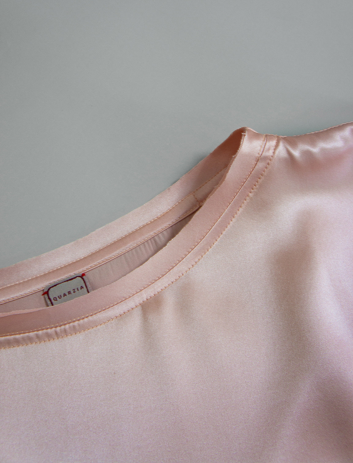 Neckline detail. Slightly cropped boxy 100% silk stretch t-shirt in soft pink with raw cut detail on neckline and sleeves.