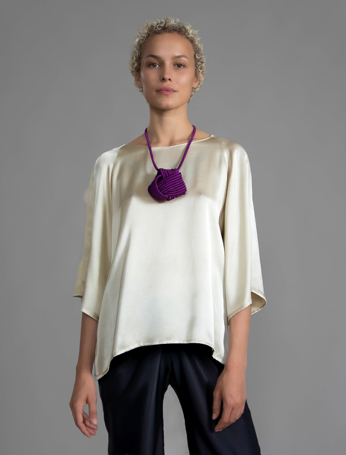 Close view. Lightweight 100% silk satin top in ivory colour, features a wide neckline with a button fastening at the back, a gently curved hemline and wide sleeves 3/4 length sleeves.