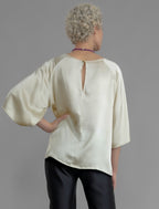 Back view. Lightweight 100% silk satin top in ivory colour, features a wide neckline with a button fastening at the back, a gently curved hemline and wide sleeves 3/4 length sleeves.