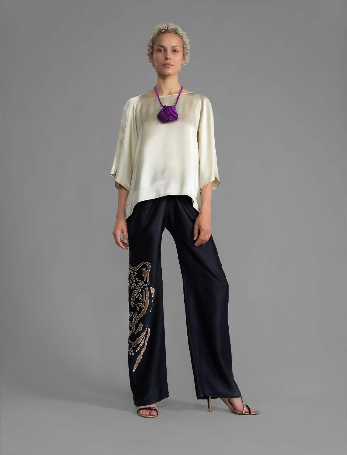 Front view. Lightweight 100% silk satin top in ivory colour, features a wide neckline with a button fastening at the back, a gently curved hemline and wide sleeves 3/4 length sleeves.