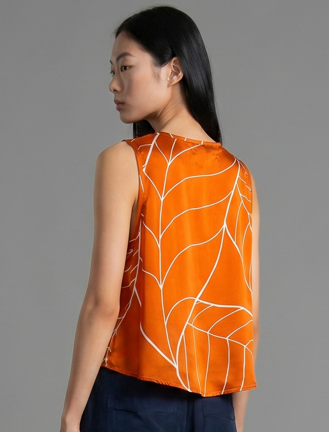 Back view. 100% silk short length stretch singlet with linear leaf motif on orange colour with open neckline and wide shoulder straps.