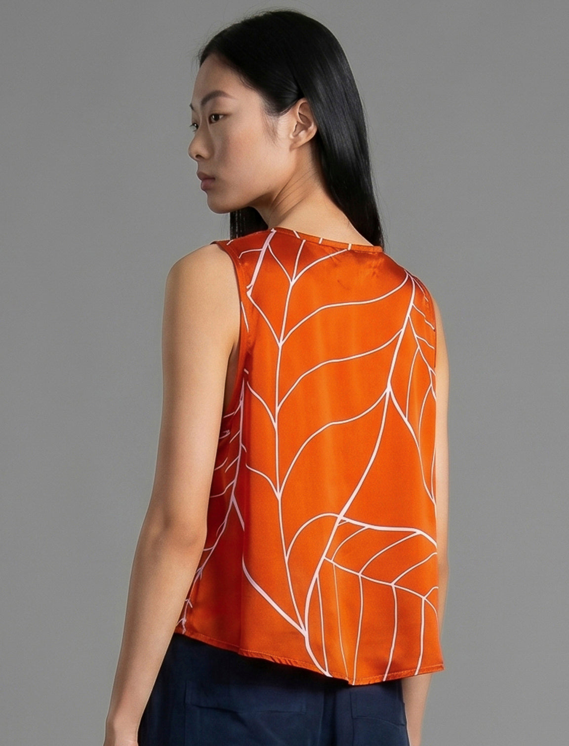 Back view. 100% silk short length stretch singlet with linear leaf motif on orange colour with open neckline and wide shoulder straps.