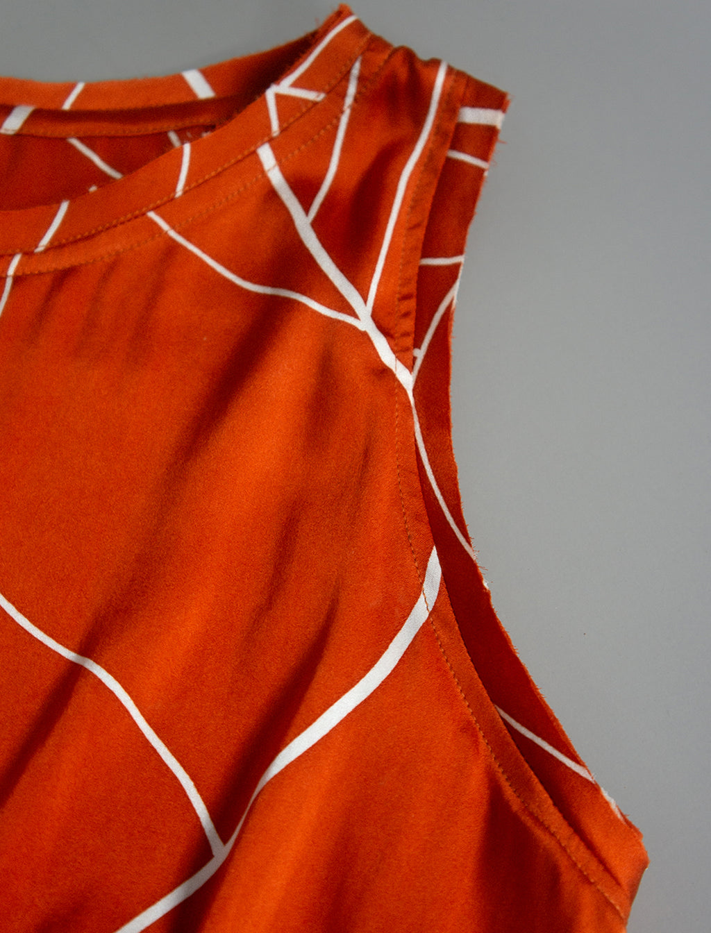 Detail view. 100% silk short length stretch singlet with linear leaf motif on orange colour with open neckline and wide shoulder straps.