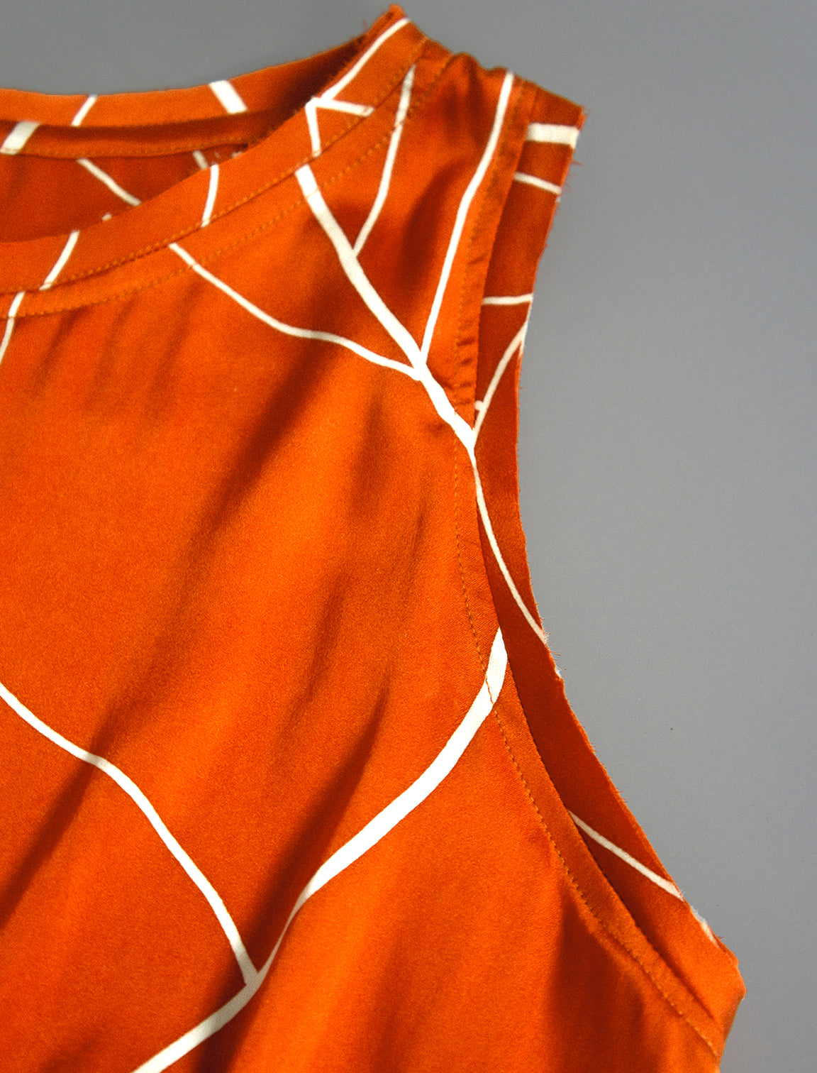 Neckline and sleeve detail. 100% silk short length stretch singlet with linear leaf motif on orange colour with open neckline and wide shoulder straps.