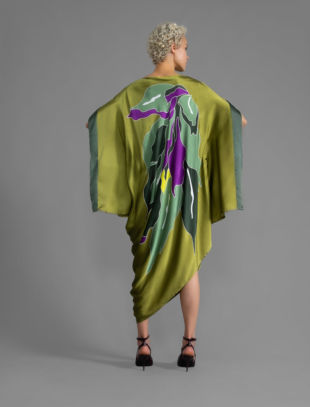 Back view. Elegant silk kaftan dress with oversized tropical leaf motif in moss green color silk, featuring flowing kimono sleeves, asymmetrical hemline, and relaxed contemporary silhouette.
