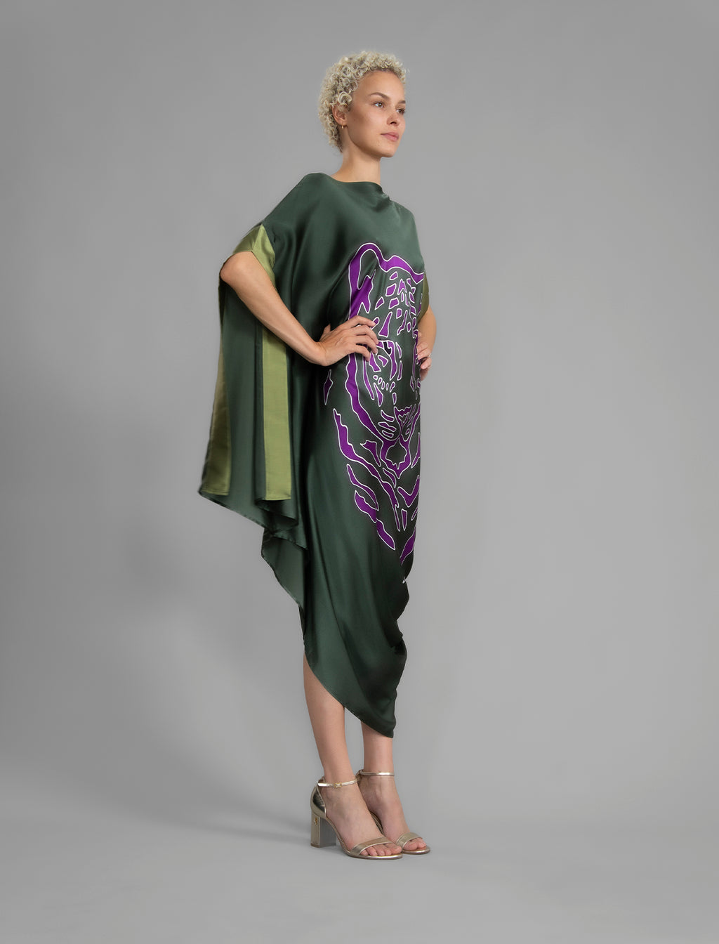 Side View. Forest green silk batik dress with bold handmade Tiger batik motif in purple, draped silhouette and artisanal craftsmanship from Bali.