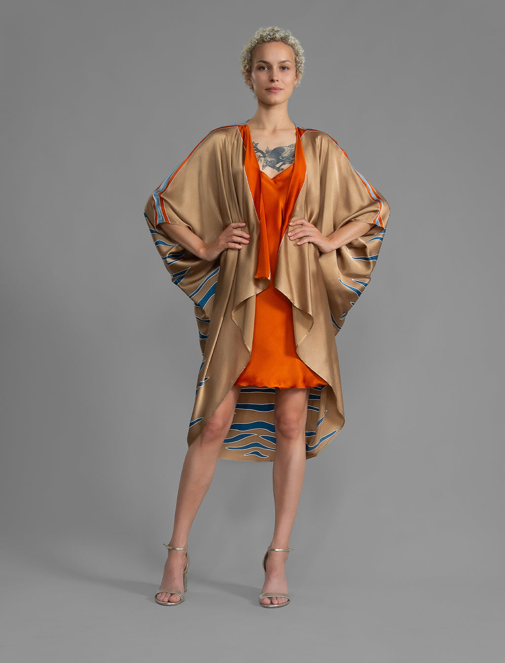 Front view. Relaxed flowing silk kaftan with graphic pale blue zebra motif on caramel colour, with orange detail, featuring 3/4 length sleeves and a voluminous silhouette.