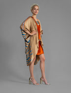 Side view. Relaxed flowing silk kaftan with graphic pale blue zebra motif on caramel colour, with orange detail, featuring 3/4 length sleeves and a voluminous silhouette.