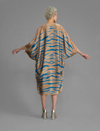 Back view. Relaxed flowing silk kaftan with graphic pale blue zebra motif on caramel colour, with orange detail, featuring 3/4 length sleeves and a voluminous silhouette.