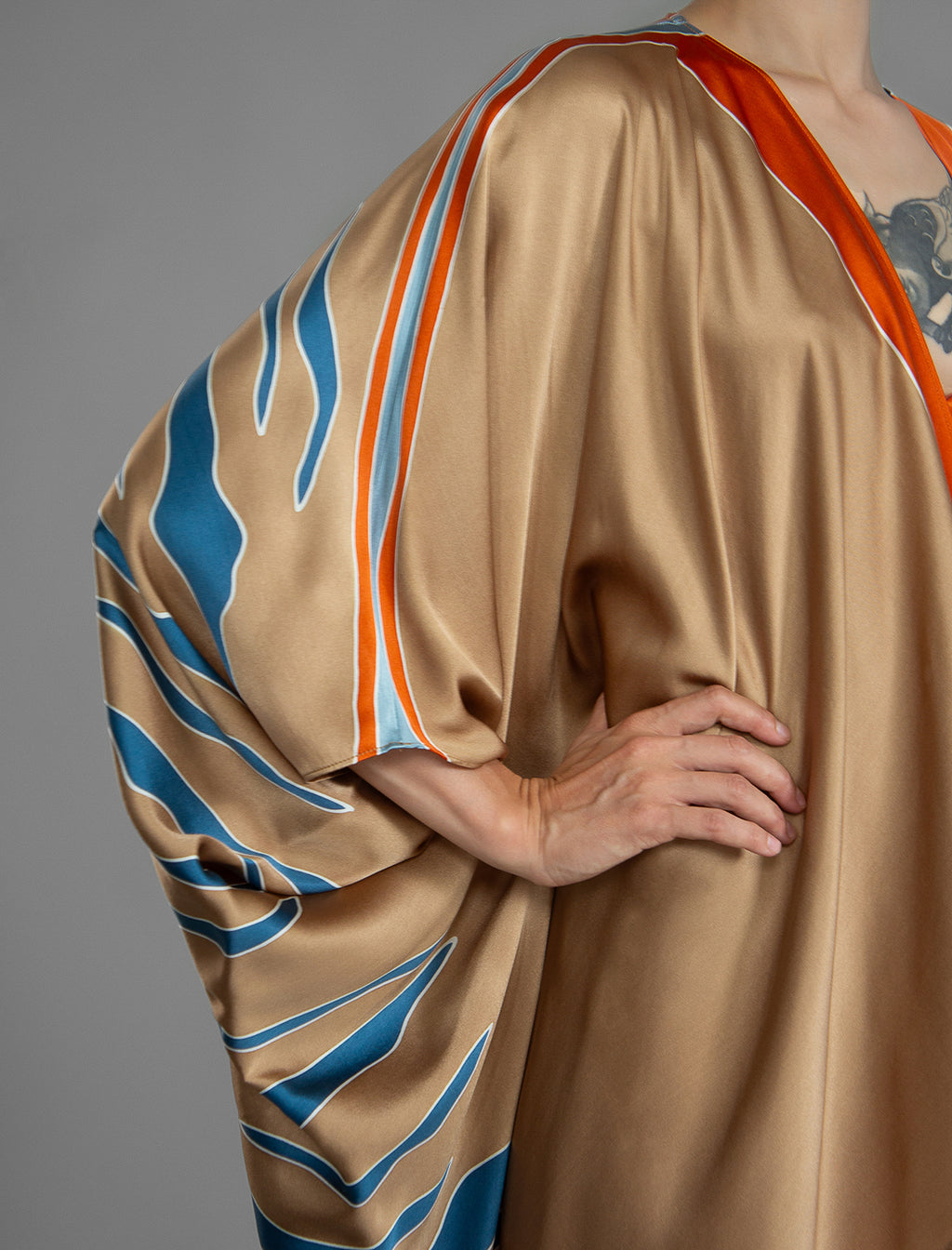 Sleeve detail. Relaxed flowing silk kaftan with graphic pale blue zebra motif on caramel colour, with orange detail, featuring 3/4 length sleeves and a voluminous silhouette.
