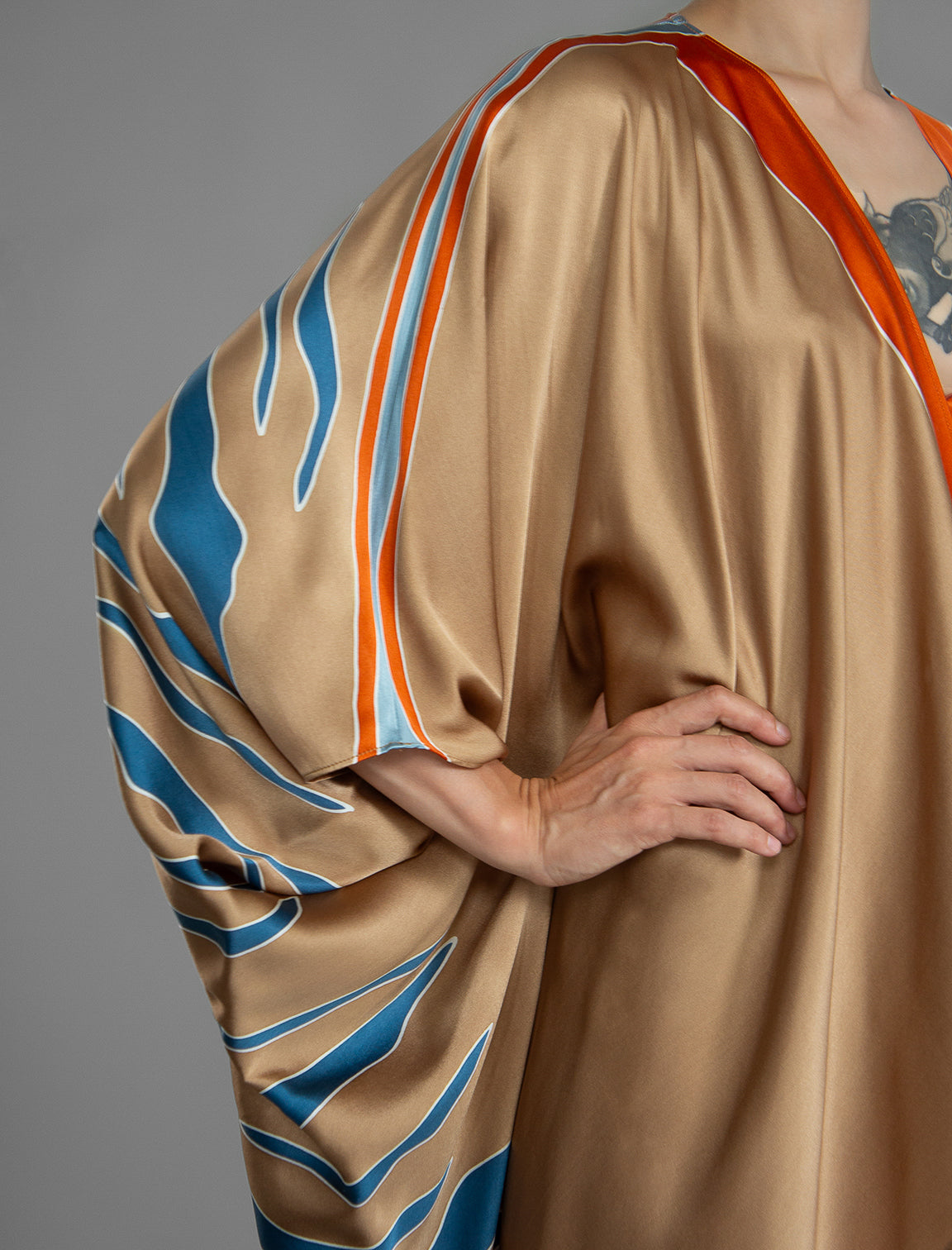 Sleeve detail. Relaxed flowing silk kaftan with graphic pale blue zebra motif on caramel colour, with orange detail, featuring 3/4 length sleeves and a voluminous silhouette.