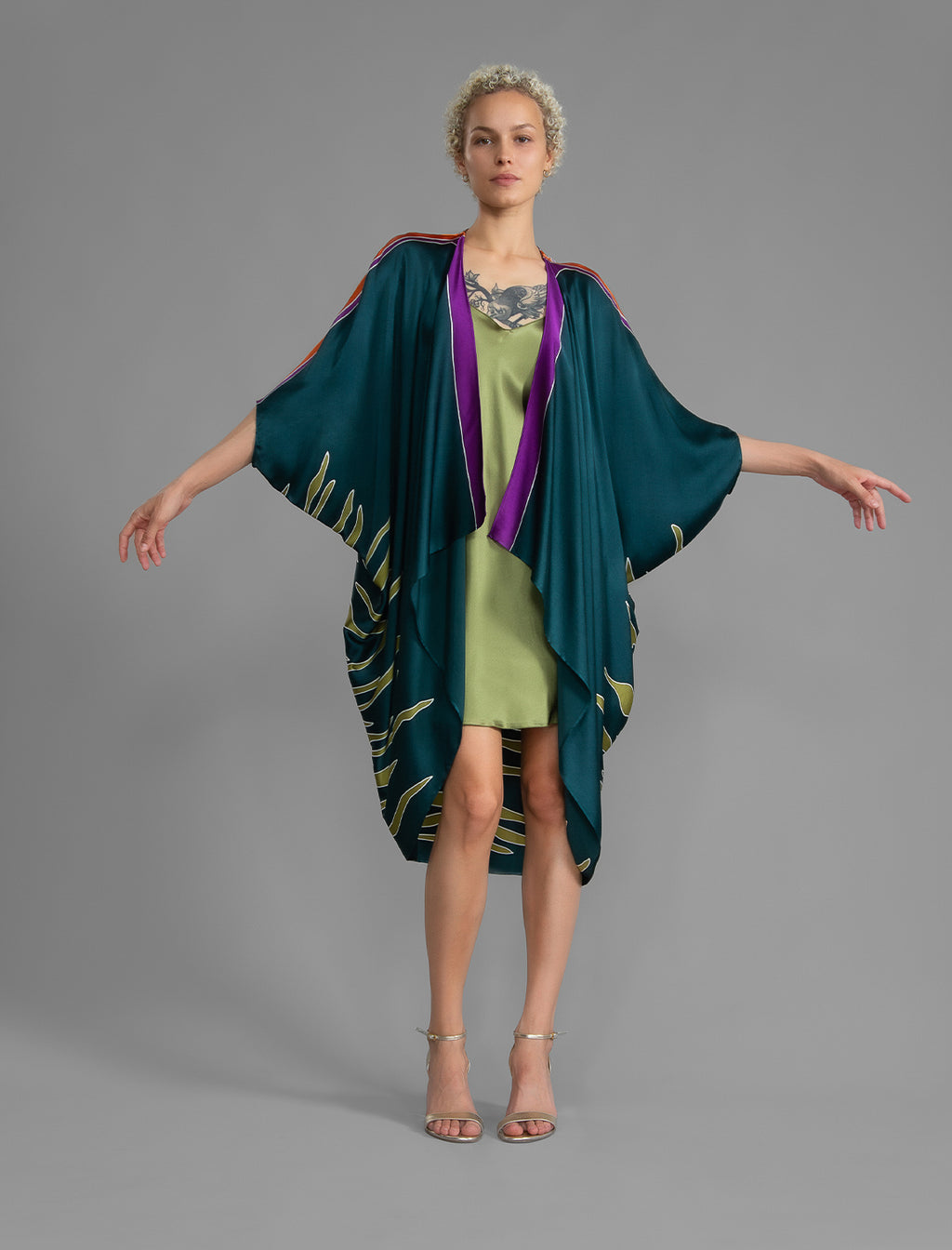 Front view. Relaxed flowing silk kaftan with graphic light green zebra motif on teal colour, with purple detail, featuring 3/4 length sleeves and a voluminous silhouette.
