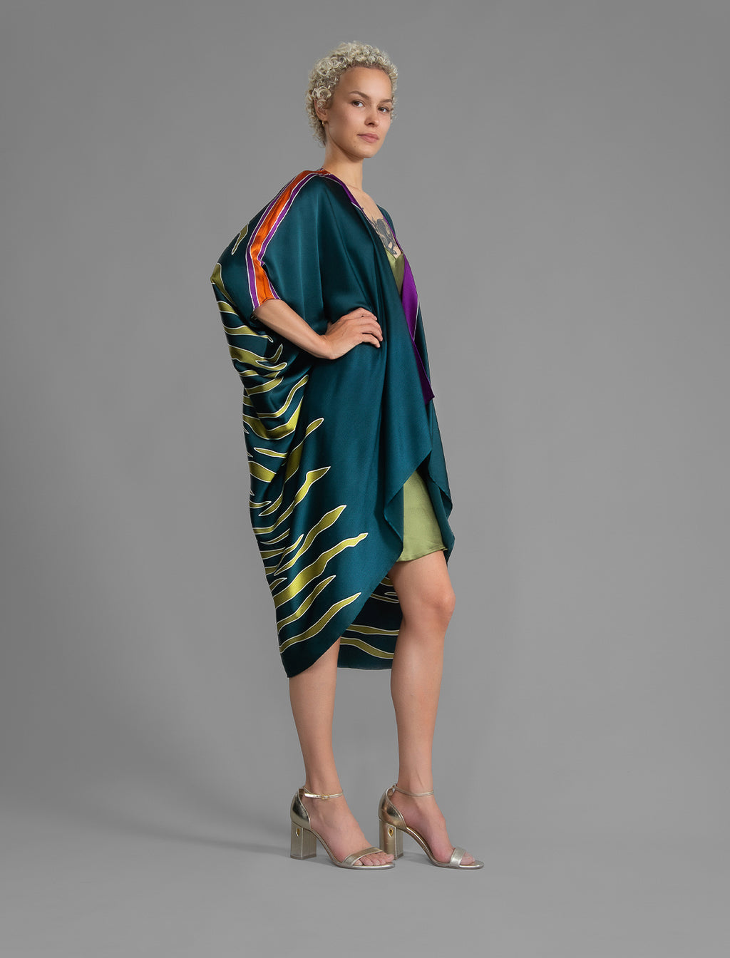Side view. Relaxed flowing silk kaftan with graphic light green zebra motif on teal colour, with purple detail, featuring 3/4 length sleeves and a voluminous silhouette.