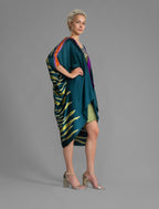Side view. Relaxed flowing silk kaftan with graphic light green zebra motif on teal colour, with purple detail, featuring 3/4 length sleeves and a voluminous silhouette.