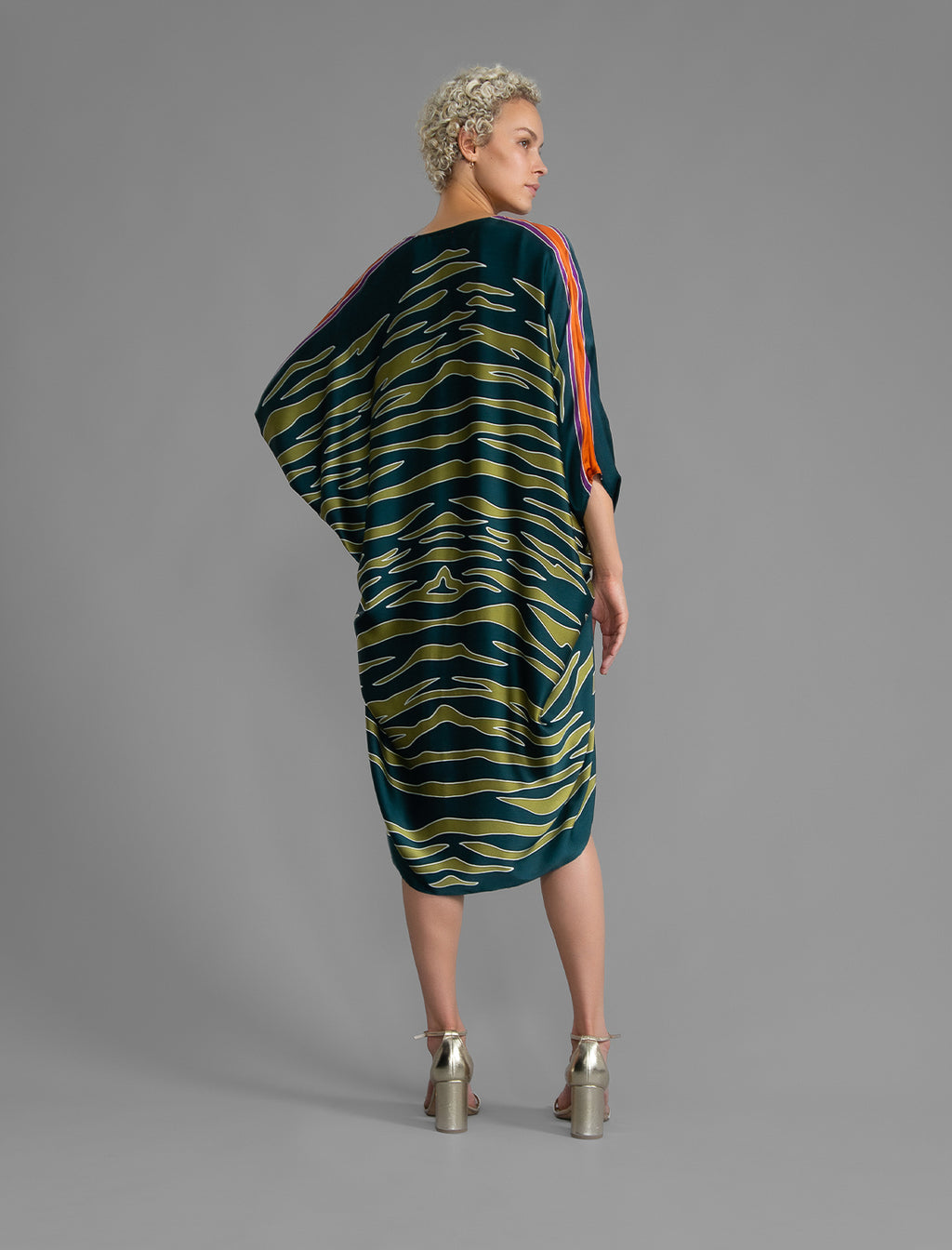 Back view. Relaxed flowing silk kaftan with graphic light green zebra motif on teal colour, with purple detail, featuring 3/4 length sleeves and a voluminous silhouette.