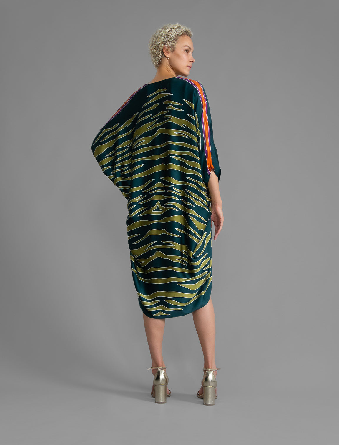 Back view. Relaxed flowing silk kaftan with graphic light green zebra motif on teal colour, with purple detail, featuring 3/4 length sleeves and a voluminous silhouette.