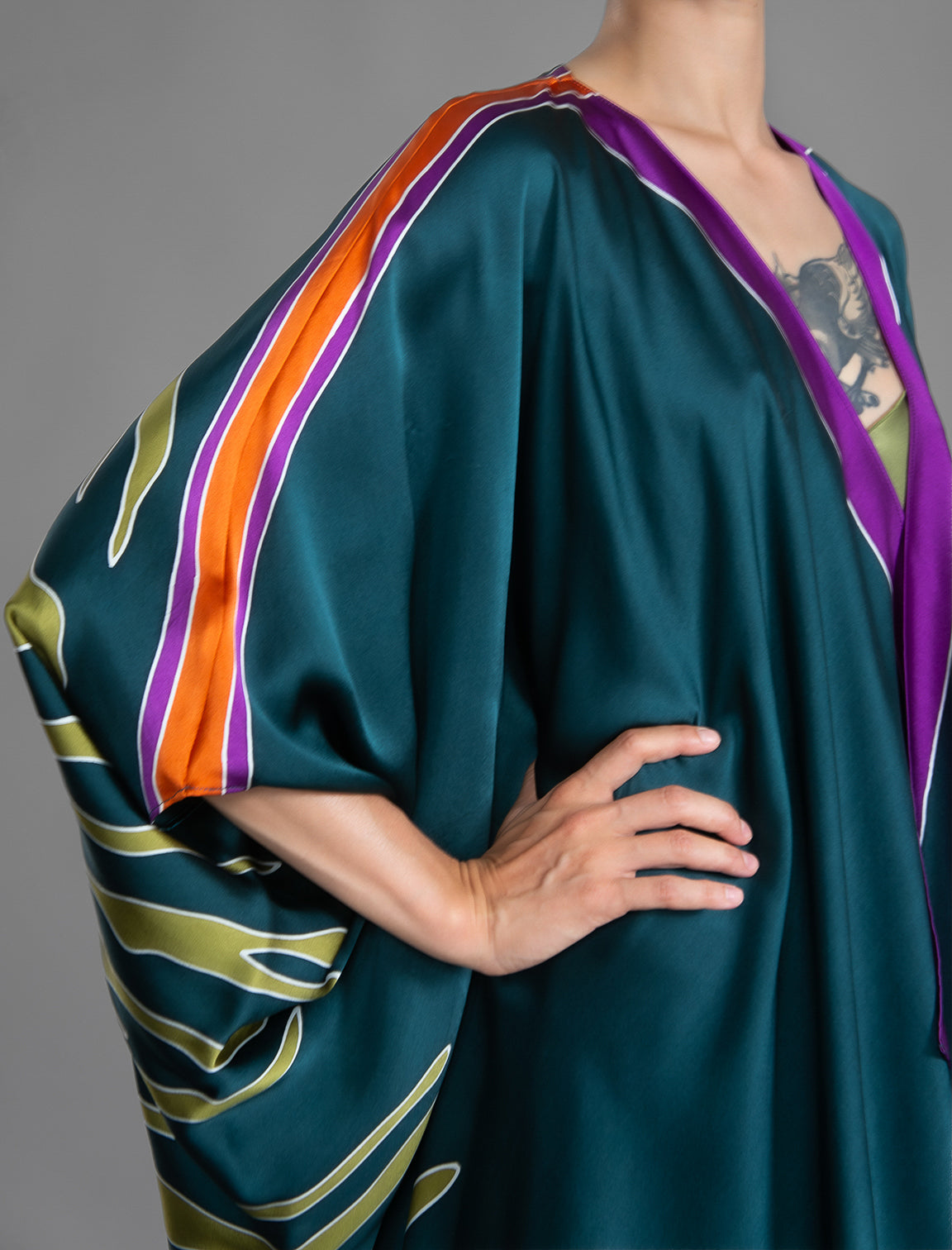 Sleeve detail. Relaxed flowing silk kaftan with graphic light green zebra motif on teal colour, with purple detail, featuring 3/4 length sleeves and a voluminous silhouette.