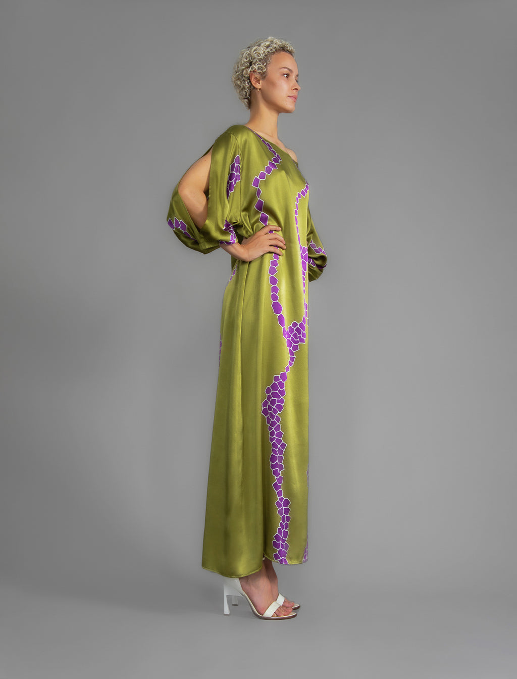 Side view. Full length 100% silk tunic dress with purple macrosnake motif on moss green colour, featuring a open, wide neckline and one side split on the skirt, gathered 3/4 length sleeves with a slash opening and optional ribbon belt.