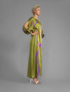 Side view. Full length 100% silk tunic dress with purple macrosnake motif on moss green colour, featuring a open, wide neckline and one side split on the skirt, gathered 3/4 length sleeves with a slash opening and optional ribbon belt.