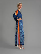 Side view. Full length 100% silk tunic dress with blue zebra motif and orange details on navy blue colour, featuring a open, wide neckline and one side split on the skirt, gathered 3/4 length sleeves with a slash opening and optional ribbon belt.