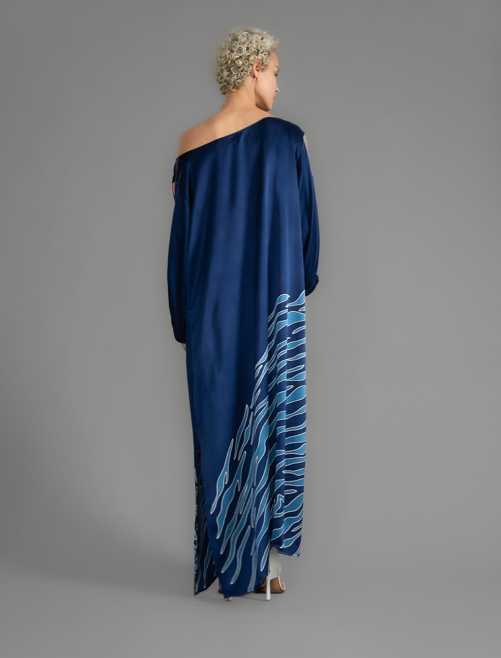 Back view. Full length 100% silk tunic dress with blue zebra motif and orange details on navy blue colour, featuring a open, wide neckline and one side split on the skirt, gathered 3/4 length sleeves with a slash opening and optional ribbon belt.