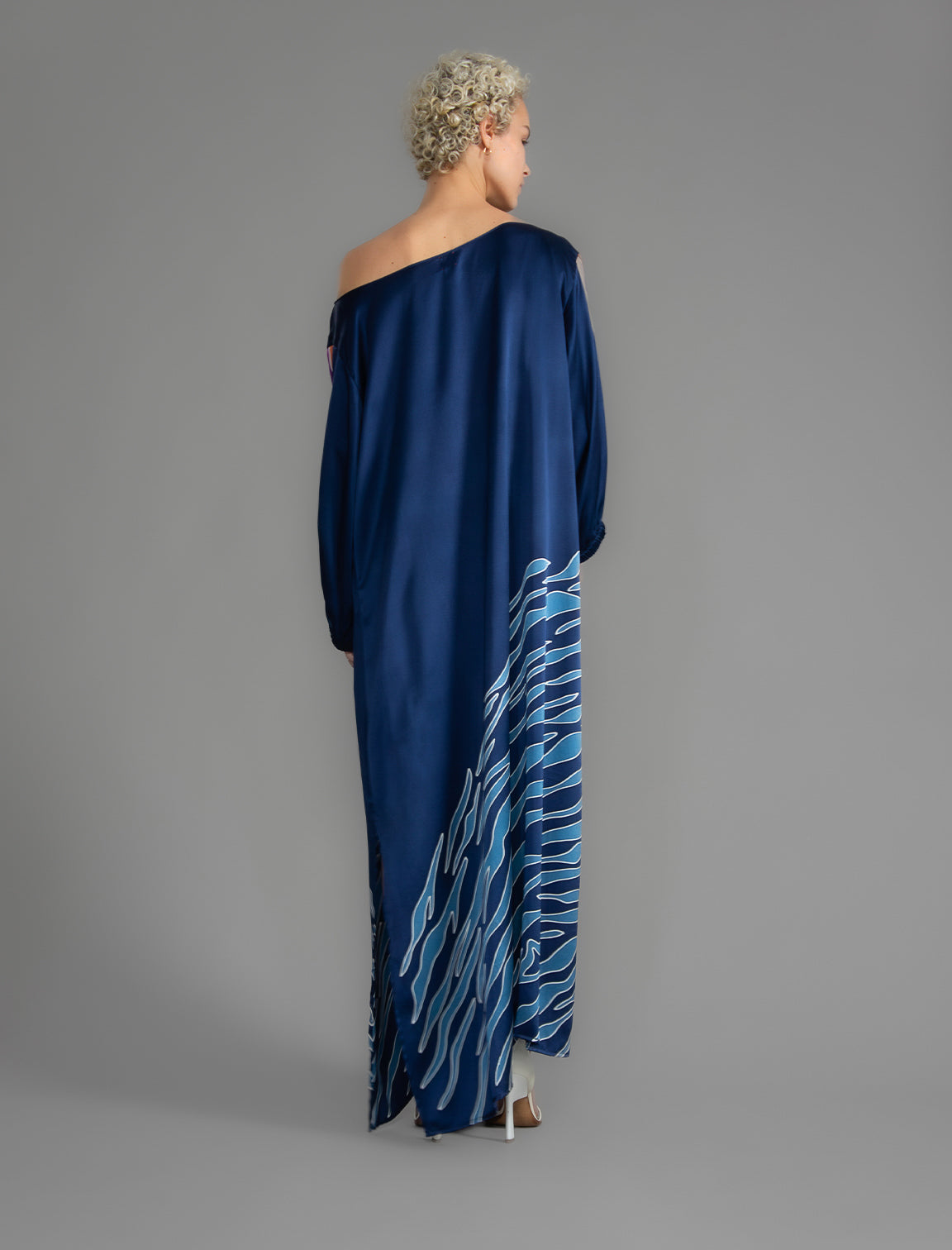 Back view. Full length 100% silk tunic dress with blue zebra motif and orange details on navy blue colour, featuring a open, wide neckline and one side split on the skirt, gathered 3/4 length sleeves with a slash opening and optional ribbon belt.