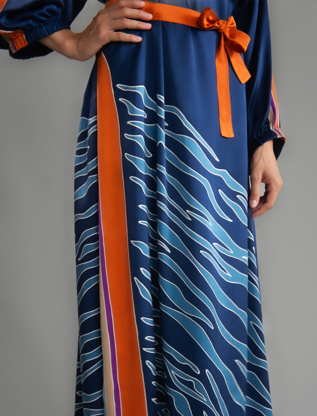 Detail view. Full length 100% silk tunic dress with blue zebra motif and orange details on navy blue colour, featuring a open, wide neckline and one side split on the skirt, gathered 3/4 length sleeves with a slash opening and optional ribbon belt.