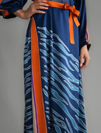 Detail view. Full length 100% silk tunic dress with blue zebra motif and orange details on navy blue colour, featuring a open, wide neckline and one side split on the skirt, gathered 3/4 length sleeves with a slash opening and optional ribbon belt.