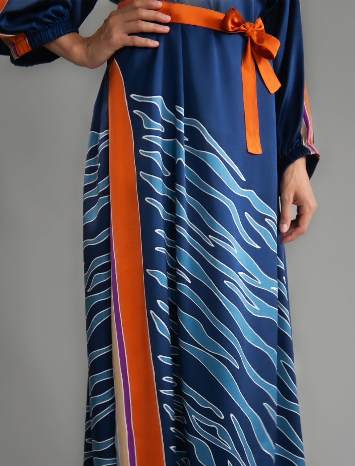 Detail view. Full length 100% silk tunic dress with blue zebra motif and orange details on navy blue colour, featuring a open, wide neckline and one side split on the skirt, gathered 3/4 length sleeves with a slash opening and optional ribbon belt.