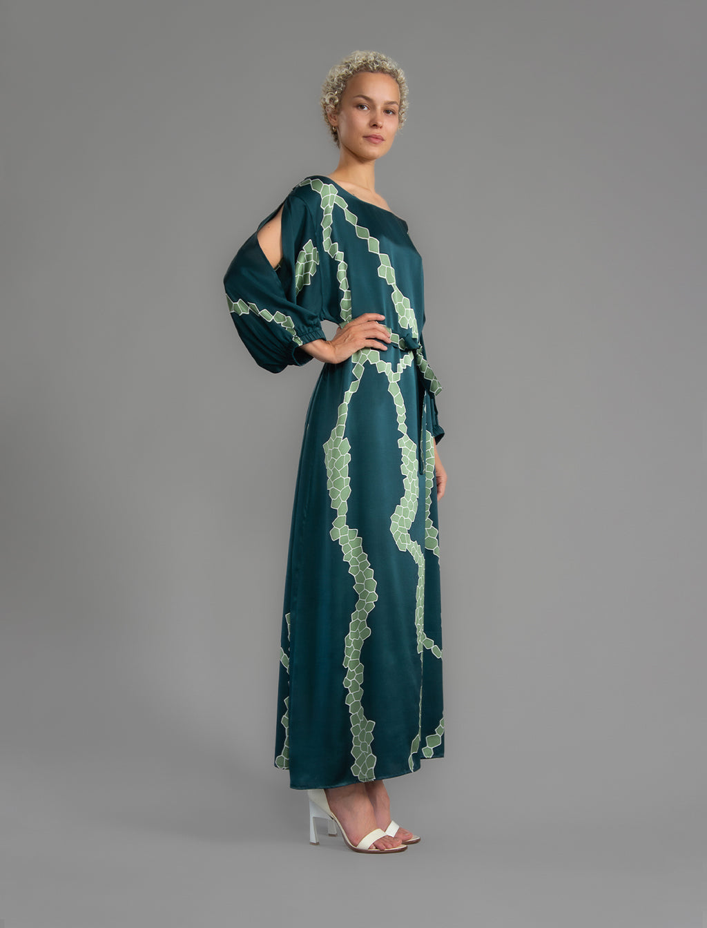 Side view. Full length 100% silk tunic dress with light green macrosnake motif on teal colour, featuring a open, wide neckline and one side split on the skirt, gathered 3/4 length sleeves with a slash opening and optional ribbon belt.