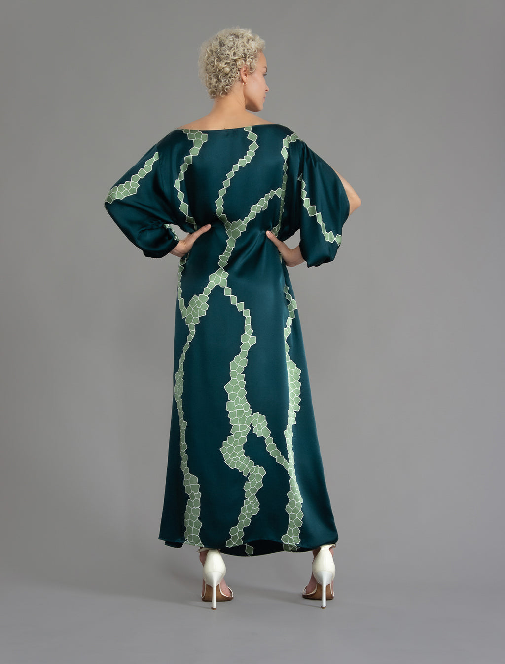 Back view. Full length 100% silk tunic dress with light green macrosnake motif on teal colour, featuring a open, wide neckline and one side split on the skirt, gathered 3/4 length sleeves with a slash opening and optional ribbon belt.