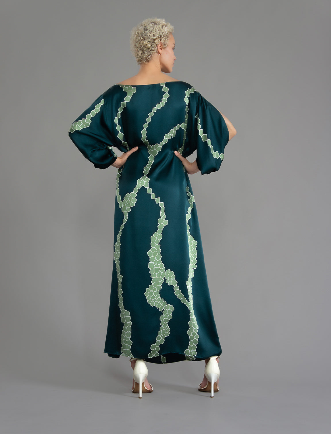 Back view. Full length 100% silk tunic dress with light green macrosnake motif on teal colour, featuring a open, wide neckline and one side split on the skirt, gathered 3/4 length sleeves with a slash opening and optional ribbon belt.