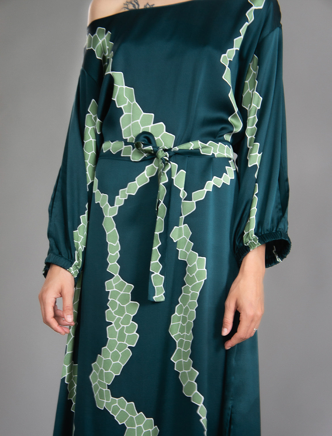 Detail view. Full length 100% silk tunic dress with light green macrosnake motif on teal colour, featuring a open, wide neckline and one side split on the skirt, gathered 3/4 length sleeves with a slash opening and optional ribbon belt.