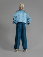 Back view. Super lightweight 100% habutai silk pant in soft mid blue, with wide leg, drawstring gather at the ankle, a deep jersey waistband with a drawstring and patch pockets on the back.