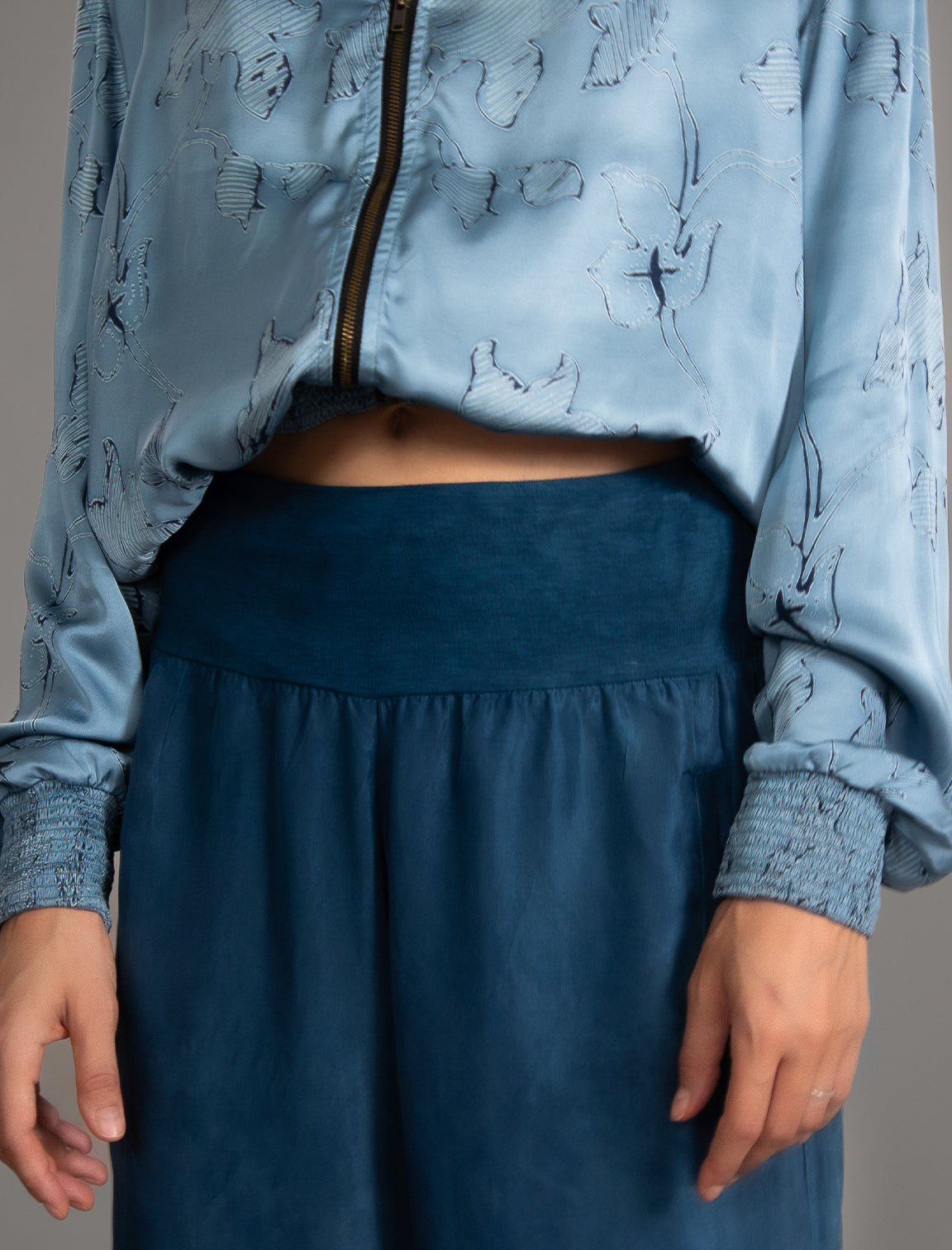 Waist detail. Super lightweight 100% habutai silk pant in soft mid blue, with wide leg, drawstring gather at the ankle, a deep jersey waistband with a drawstring and patch pockets on the back.