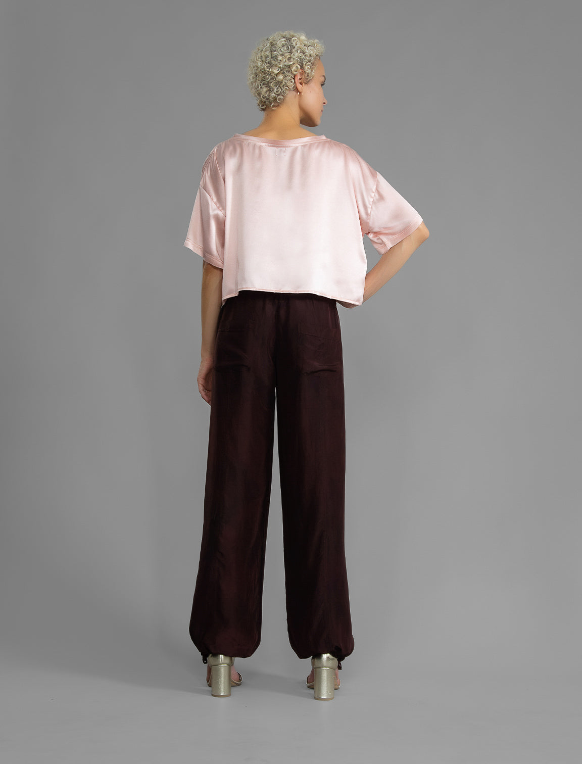 Back view. Super lightweight 100% habutai silk pant in warm brown, with wide leg, drawstring gather at the ankle, a deep jersey waistband with a drawstring and patch pockets on the back.