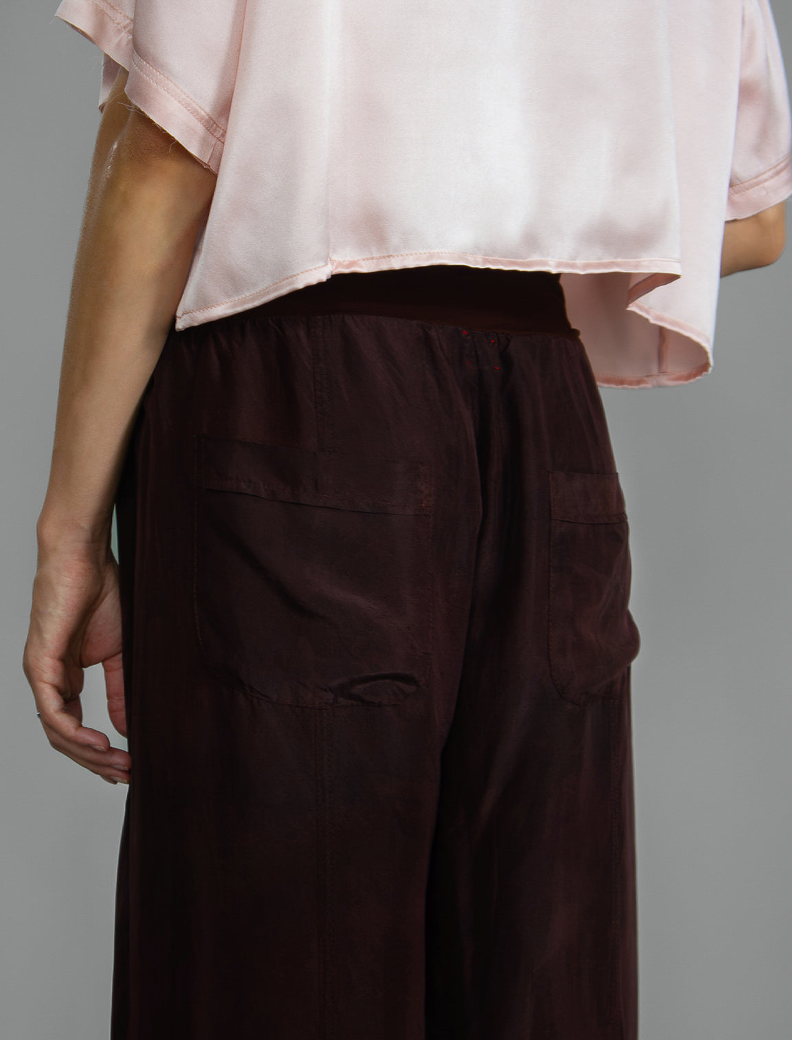 Pocket detail. Super lightweight 100% habutai silk pant in warm brown, with wide leg, drawstring gather at the ankle, a deep jersey waistband with a drawstring and patch pockets on the back.