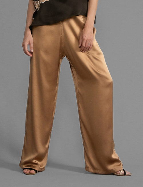 Close front view. Relaxed wide-leg silk trousers in warm tobacco, featuring drawstring waistband, elasticated at the back. Soft gathered drape, fluid silhouette, and subtle lustrous finish.