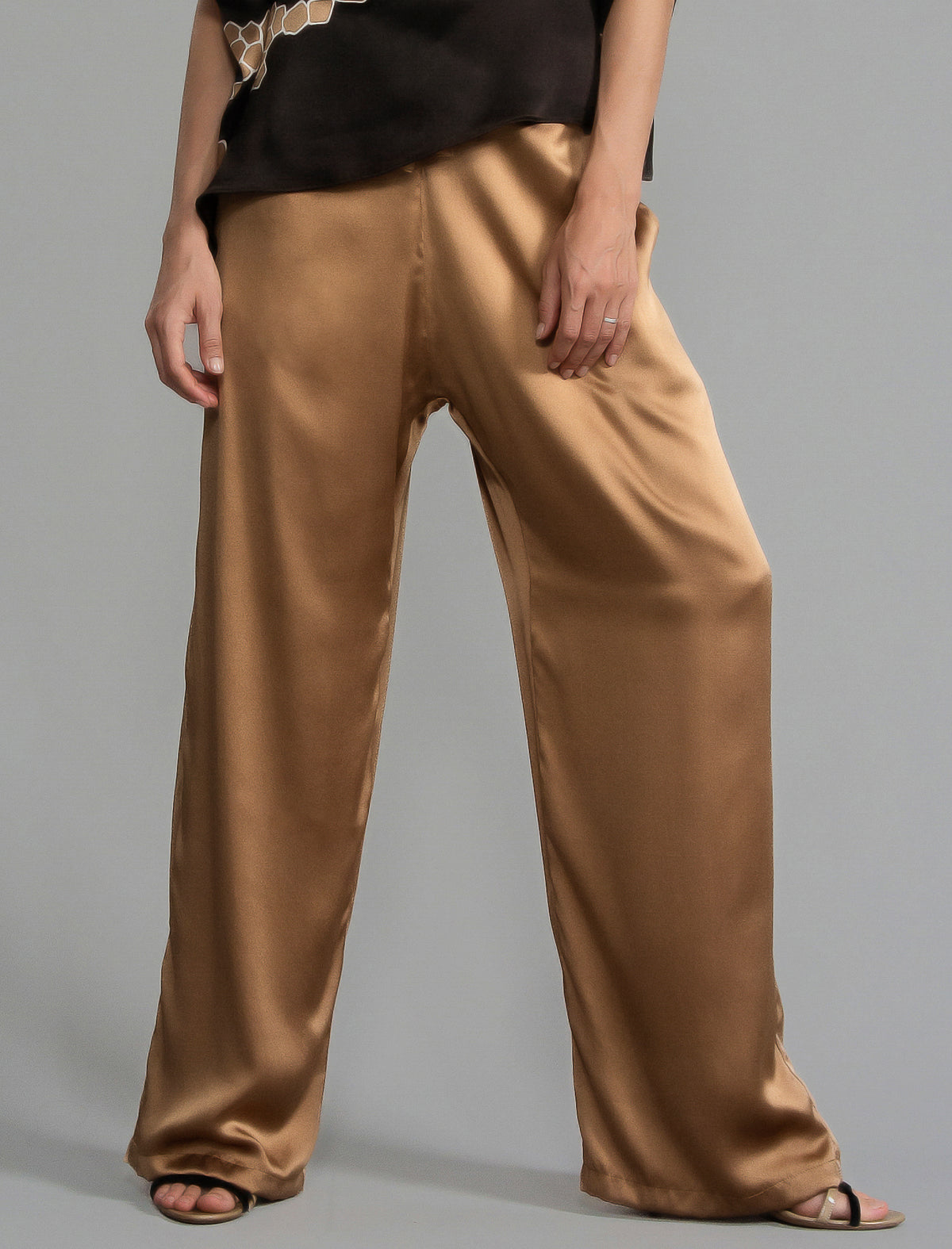 Close front view. Relaxed wide-leg silk trousers in warm tobacco, featuring drawstring waistband, elasticated at the back. Soft gathered drape, fluid silhouette, and subtle lustrous finish.