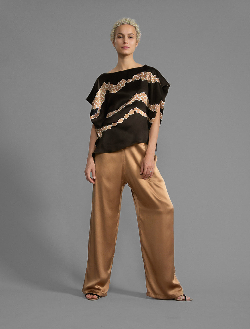 Front view. Relaxed wide-leg silk trousers in warm tobacco, featuring drawstring waistband, elasticated at the back. Soft gathered drape, fluid silhouette, and subtle lustrous finish.