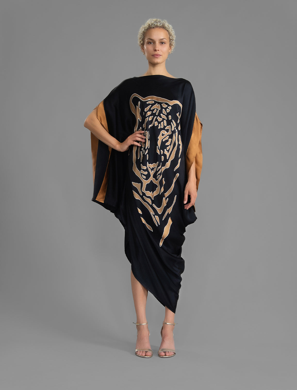 Front view. Elegant silk kaftan dress with tiger head batik motif on black color silk, featuring flowing kimono sleeves, asymmetrical hemline, and relaxed contemporary silhouette.
