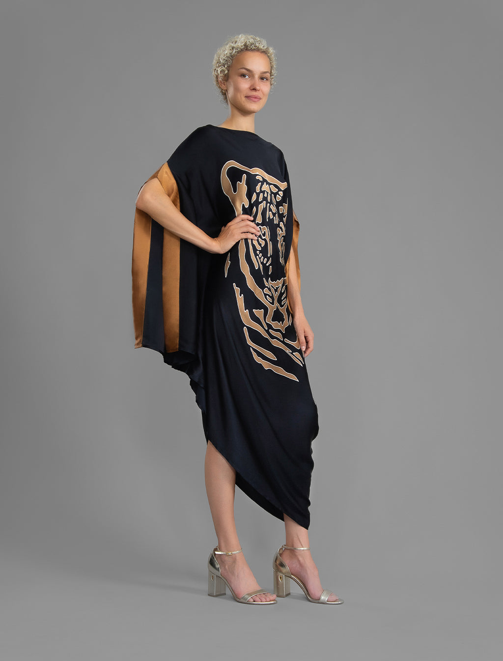 Side view. Elegant silk kaftan dress with tiger head batik motif on black color silk, featuring flowing kimono sleeves, asymmetrical hemline, and relaxed contemporary silhouette.