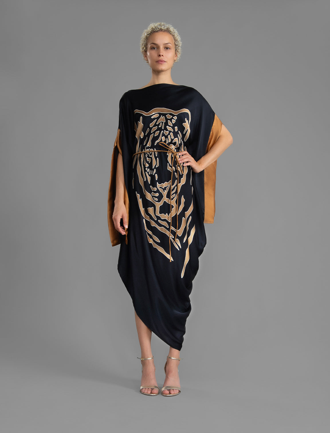 Front view with belt. Elegant silk kaftan dress with tiger head batik motif on black color silk, featuring flowing kimono sleeves, asymmetrical hemline, and relaxed contemporary silhouette.