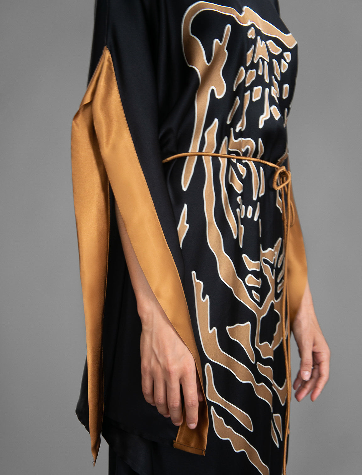 Detail view. Elegant silk kaftan dress with tiger head batik motif on black color silk, featuring flowing kimono sleeves, asymmetrical hemline, and relaxed contemporary silhouette.